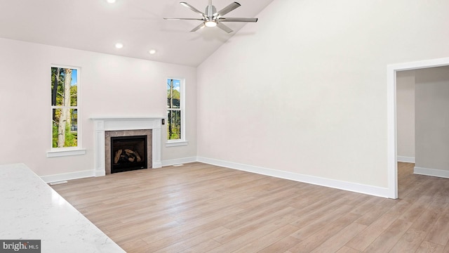 unfurnished living room with high vaulted ceiling, a tiled fireplace, ceiling fan, and light wood-type flooring