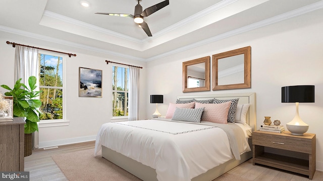 bedroom with crown molding, multiple windows, light wood-type flooring, and a tray ceiling