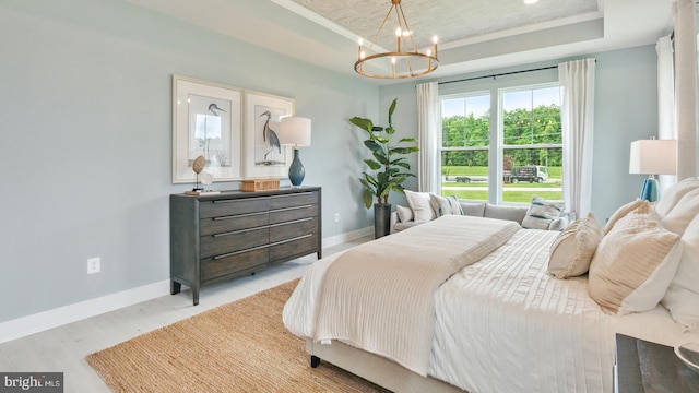 bedroom featuring light hardwood / wood-style flooring, a chandelier, and a tray ceiling