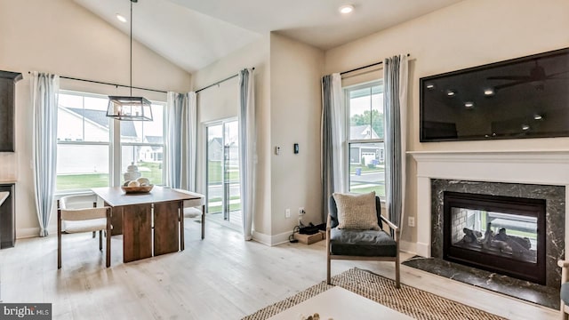 dining space featuring a premium fireplace, light hardwood / wood-style flooring, and high vaulted ceiling