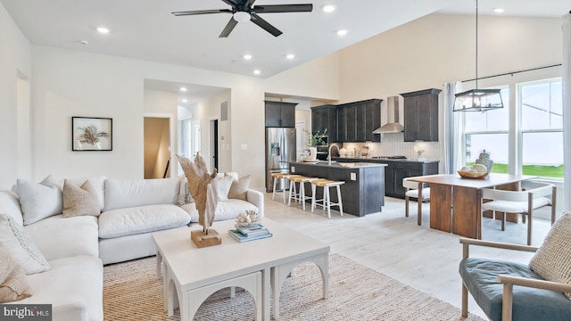 living room featuring light hardwood / wood-style flooring, sink, high vaulted ceiling, and ceiling fan