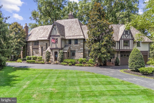 tudor house featuring a garage and a front lawn