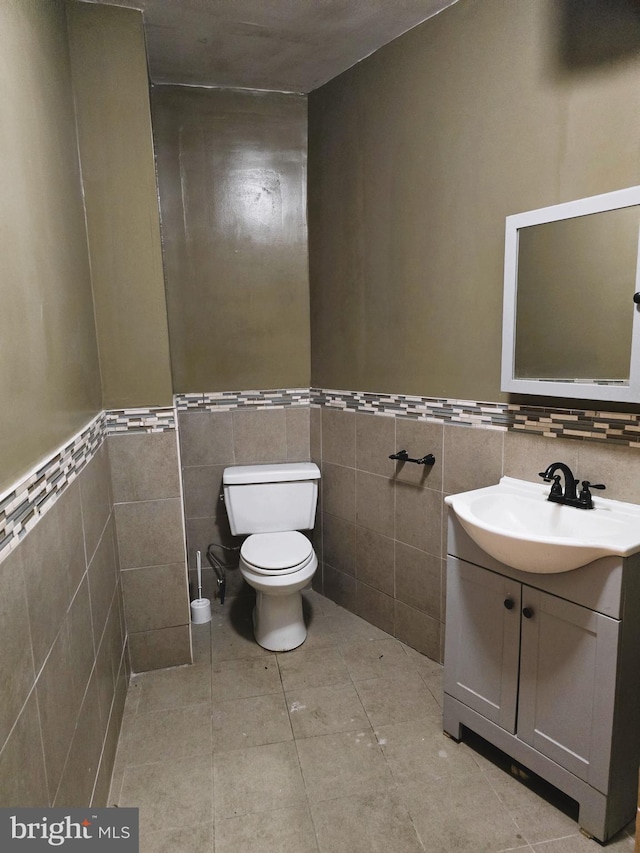 bathroom featuring toilet, vanity, tile patterned floors, and tile walls