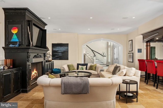 living area featuring a lit fireplace, arched walkways, stone tile flooring, and recessed lighting