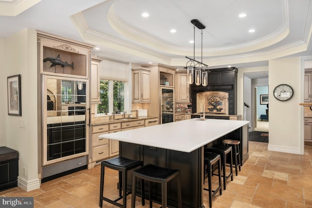 kitchen with a tray ceiling, light countertops, stone tile floors, and an island with sink