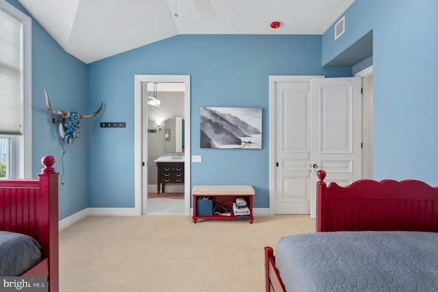 bedroom featuring light carpet, baseboards, visible vents, lofted ceiling, and ensuite bath