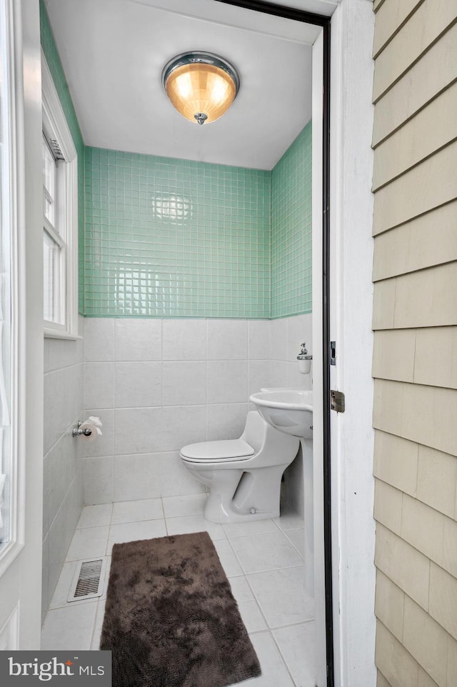 half bath with visible vents, toilet, tile patterned flooring, and tile walls