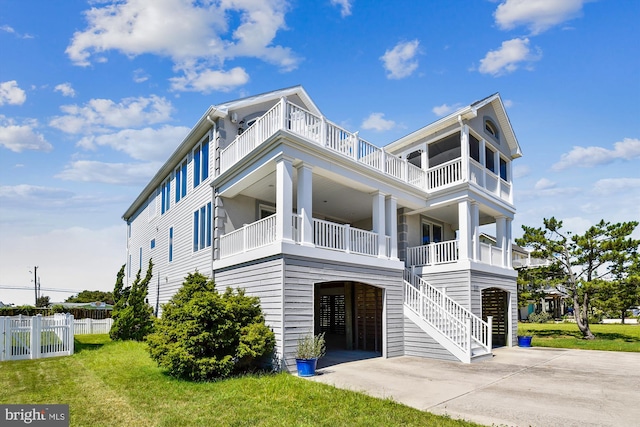 raised beach house featuring stairway, a front yard, fence, a balcony, and driveway