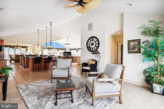 carpeted living room with ceiling fan with notable chandelier, ornate columns, and high vaulted ceiling