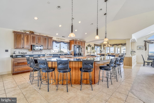 kitchen featuring brown cabinets, decorative light fixtures, a healthy amount of sunlight, a large island with sink, and black appliances