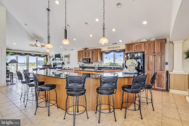 kitchen featuring freestanding refrigerator, hanging light fixtures, a breakfast bar area, and decorative columns