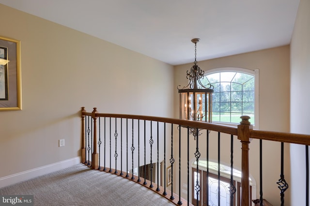 hallway with an inviting chandelier, carpet, and baseboards