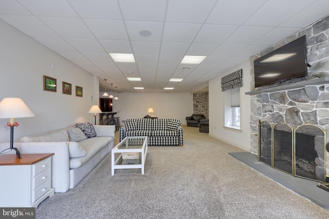 living room featuring carpet, a drop ceiling, and a stone fireplace