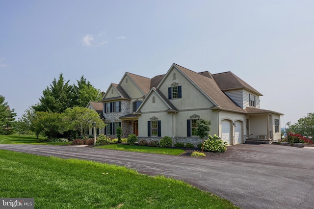 view of front of property with stucco siding, an attached garage, a front yard, stone siding, and driveway