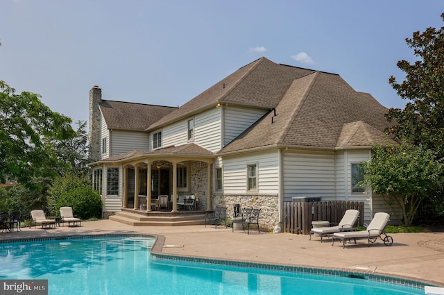 rear view of house featuring a patio, a shingled roof, fence, stone siding, and an outdoor pool