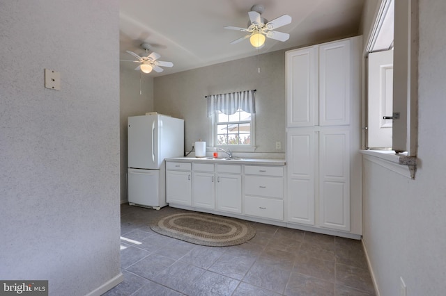 kitchen featuring freestanding refrigerator, white cabinetry, a sink, ceiling fan, and baseboards