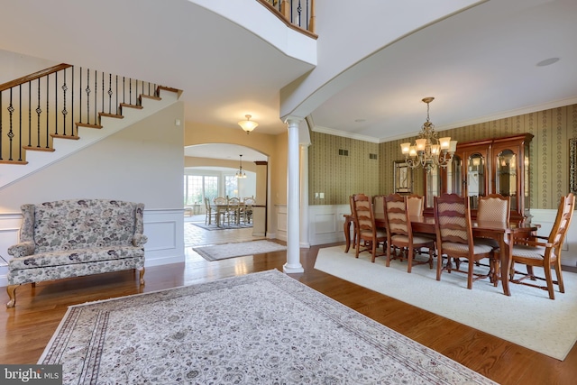 dining room featuring wallpapered walls, a chandelier, a wainscoted wall, and ornate columns