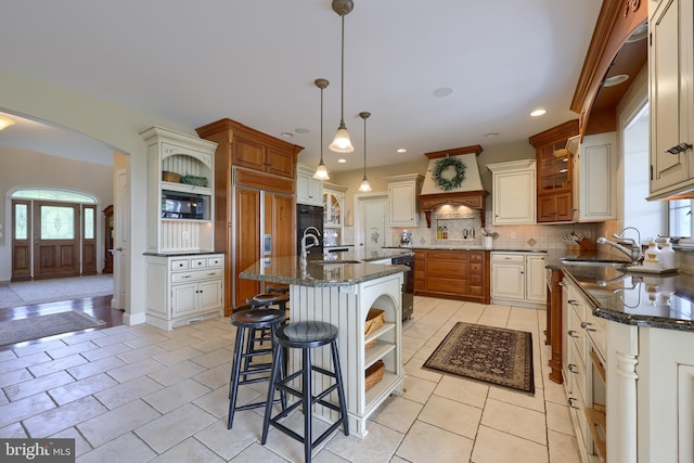 kitchen with arched walkways, open shelves, custom range hood, a sink, and built in appliances