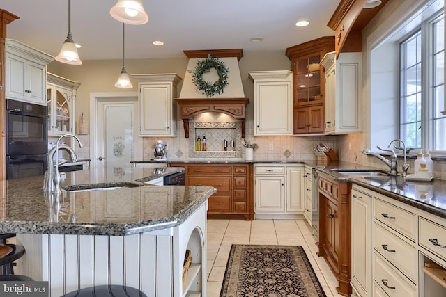 kitchen with glass insert cabinets, custom range hood, a sink, and a kitchen breakfast bar