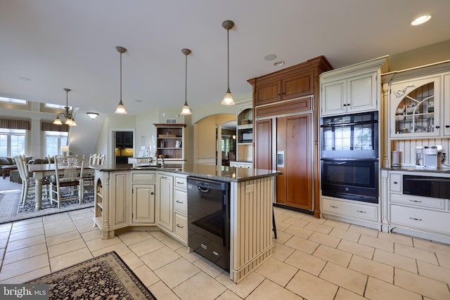 kitchen featuring arched walkways, glass insert cabinets, cream cabinets, a kitchen island with sink, and black appliances