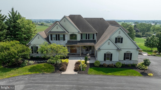 view of front of home featuring stone siding, a front lawn, a porch, and stucco siding