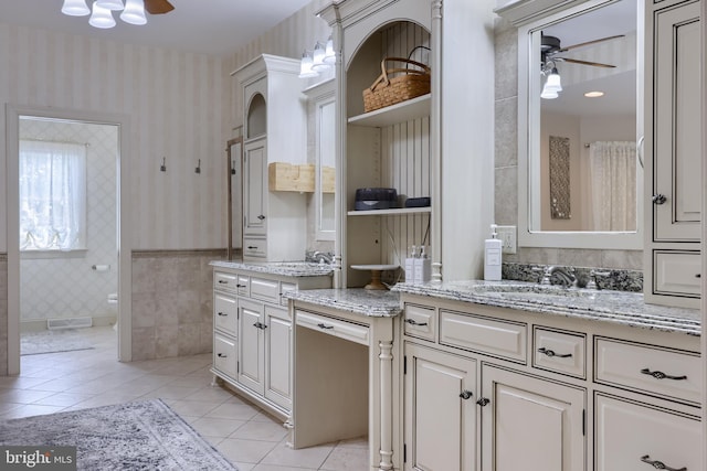 bathroom with wallpapered walls, wainscoting, ceiling fan, tile patterned floors, and vanity