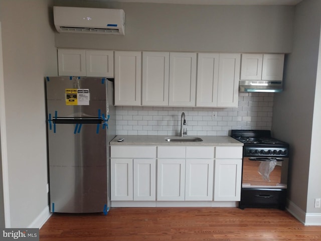 kitchen with a wall unit AC, white cabinetry, stainless steel refrigerator, and gas stove