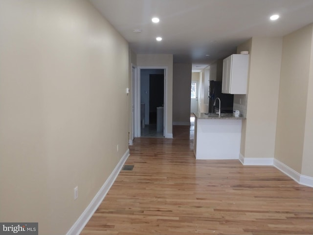 interior space with light stone countertops, black fridge, light hardwood / wood-style floors, white cabinets, and sink