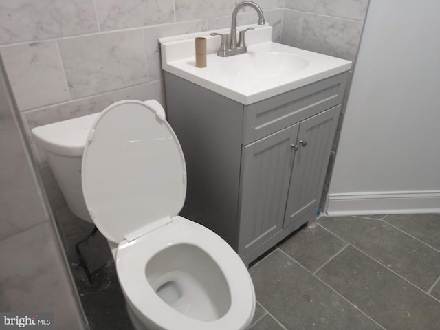 bathroom with toilet, vanity, tile patterned floors, and tile walls