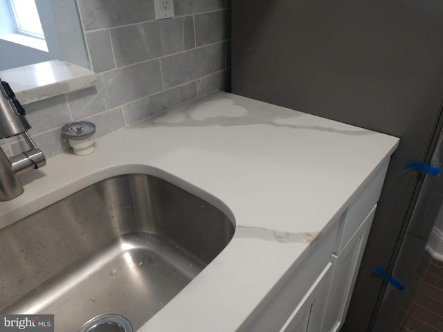 interior details featuring sink, backsplash, and light stone countertops