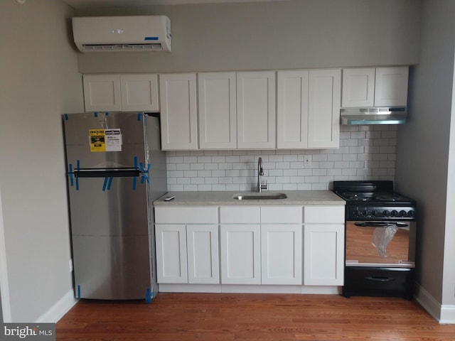 kitchen featuring a wall mounted AC, range with gas stovetop, white cabinetry, stainless steel refrigerator, and sink