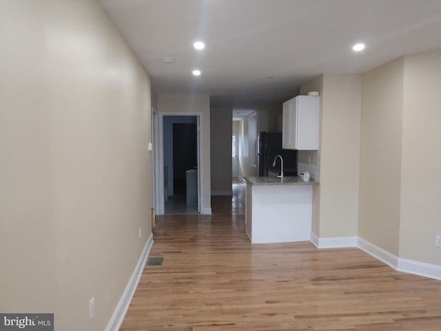 kitchen featuring white cabinets, black fridge, tasteful backsplash, light hardwood / wood-style flooring, and light stone countertops