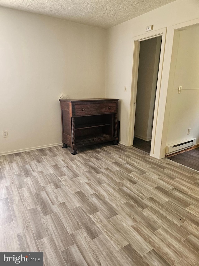 empty room with light hardwood / wood-style floors, a baseboard radiator, and a textured ceiling