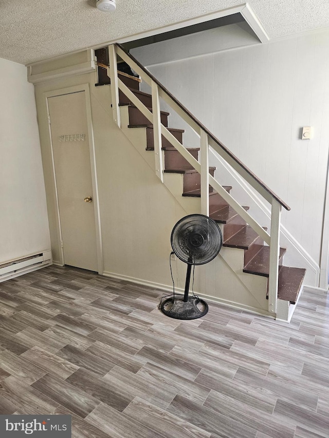 stairway with a textured ceiling, hardwood / wood-style floors, and a baseboard radiator