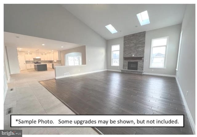 unfurnished living room with a skylight, a fireplace, hardwood / wood-style floors, and high vaulted ceiling