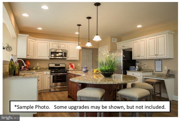 kitchen with light stone countertops, white cabinets, appliances with stainless steel finishes, a center island, and sink