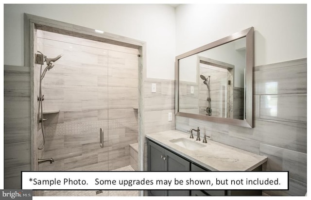 bathroom with a shower with shower door, vanity, and tile walls