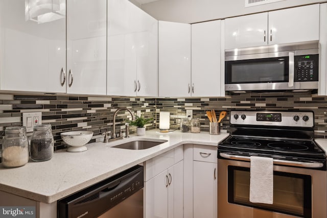 kitchen featuring white cabinets, stainless steel appliances, sink, backsplash, and light stone counters