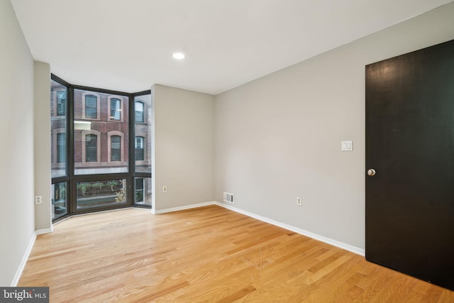 empty room with a wall of windows and light hardwood / wood-style flooring