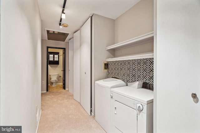 laundry area featuring track lighting, washer and clothes dryer, and light carpet