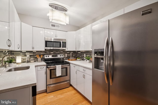 kitchen featuring appliances with stainless steel finishes, tasteful backsplash, light wood-type flooring, white cabinets, and sink