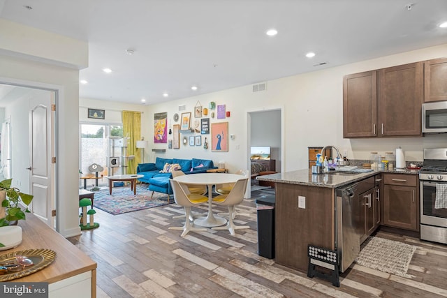 kitchen featuring appliances with stainless steel finishes, hardwood / wood-style floors, sink, kitchen peninsula, and dark stone countertops