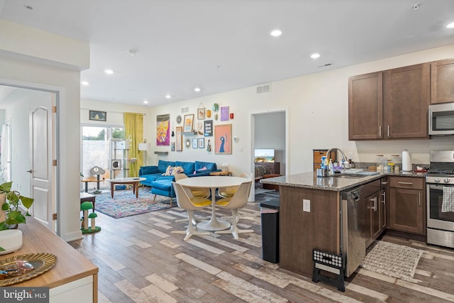 kitchen featuring sink, dark stone counters, kitchen peninsula, stainless steel appliances, and light hardwood / wood-style flooring