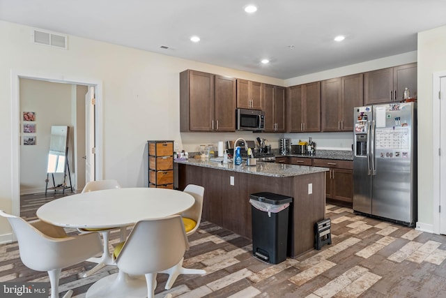 kitchen with appliances with stainless steel finishes, light hardwood / wood-style flooring, sink, light stone counters, and dark brown cabinetry