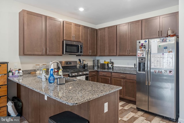 kitchen with light wood-type flooring, kitchen peninsula, stone counters, and appliances with stainless steel finishes