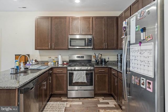 kitchen with sink, dark wood-type flooring, appliances with stainless steel finishes, kitchen peninsula, and dark stone counters