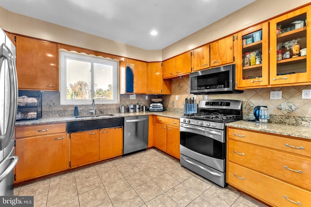 kitchen featuring stainless steel appliances, light stone countertops, sink, and decorative backsplash