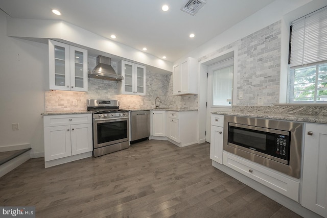 kitchen with white cabinets, wall chimney range hood, light stone counters, and appliances with stainless steel finishes