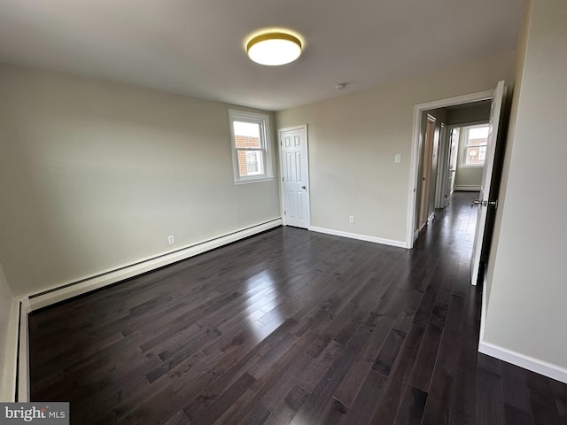 empty room with baseboard heating and dark hardwood / wood-style floors