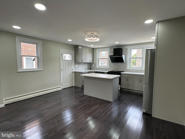 kitchen featuring wall chimney range hood, a center island, decorative backsplash, appliances with stainless steel finishes, and a baseboard radiator